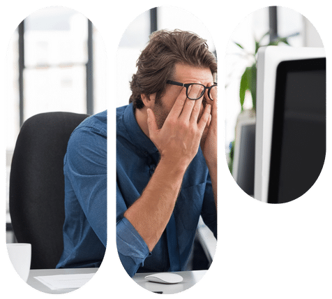 Man at office desk rubs his eyes beside a monitor, conveying screen fatigue and stress.
