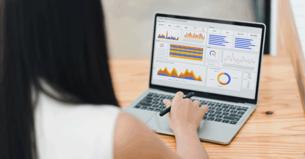 Person analyzing a sales dashboard on a laptop with bar, line, and pie charts.